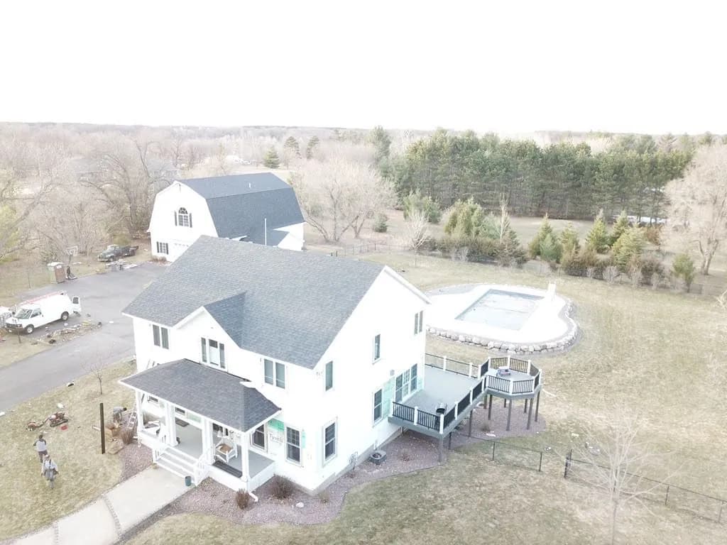 Aerial view of a white farmhouse with a new gray shingle roof and a pool alongside it