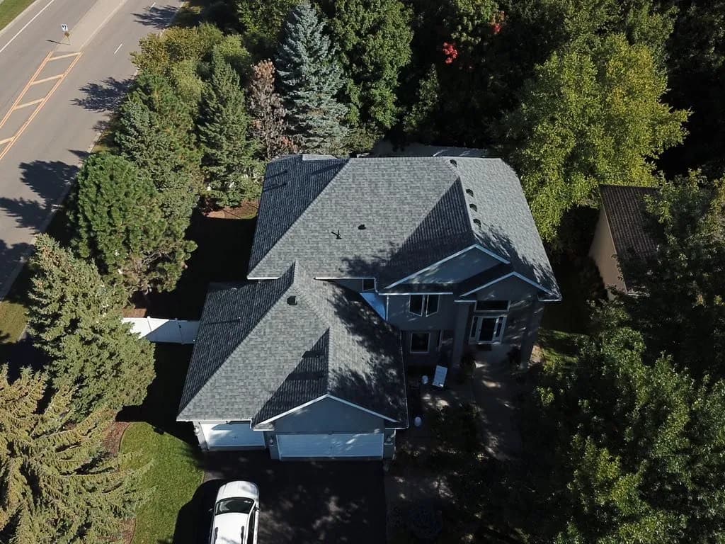 Aerial view of a large home with a new charcoal shingle roof surrounded by mature trees