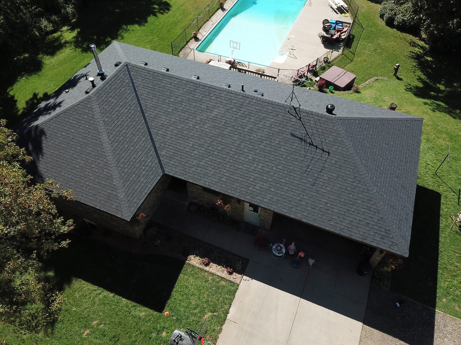 Aerial drone view of a large rambler with a new charcoal architectural shingle roof and a backyard pool