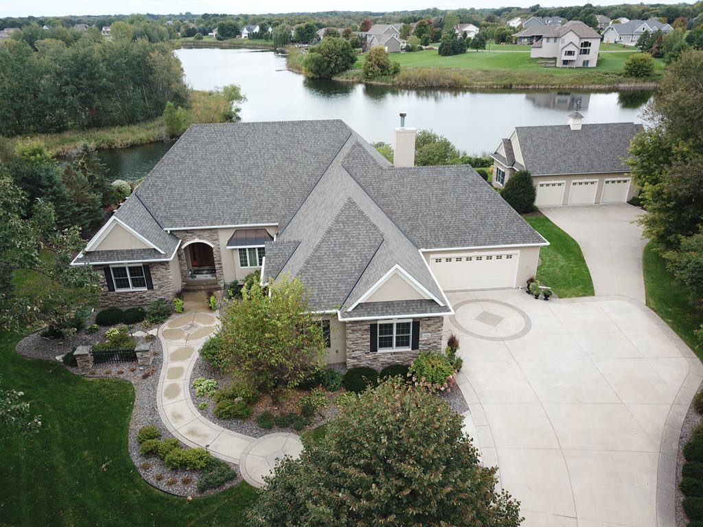 Aerial drone view of a two-story home beside a pond with a newly installed gray shingle roof