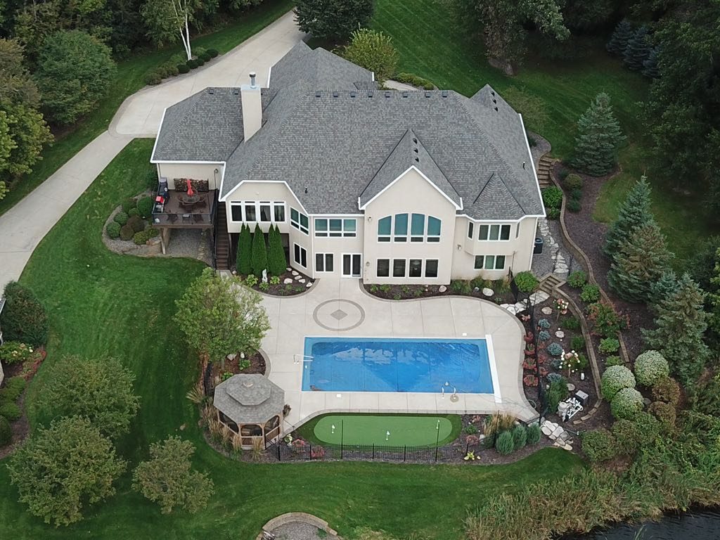 Aerial drone view of a luxury home with a new gray shingle roof, swimming pool and mature landscaping