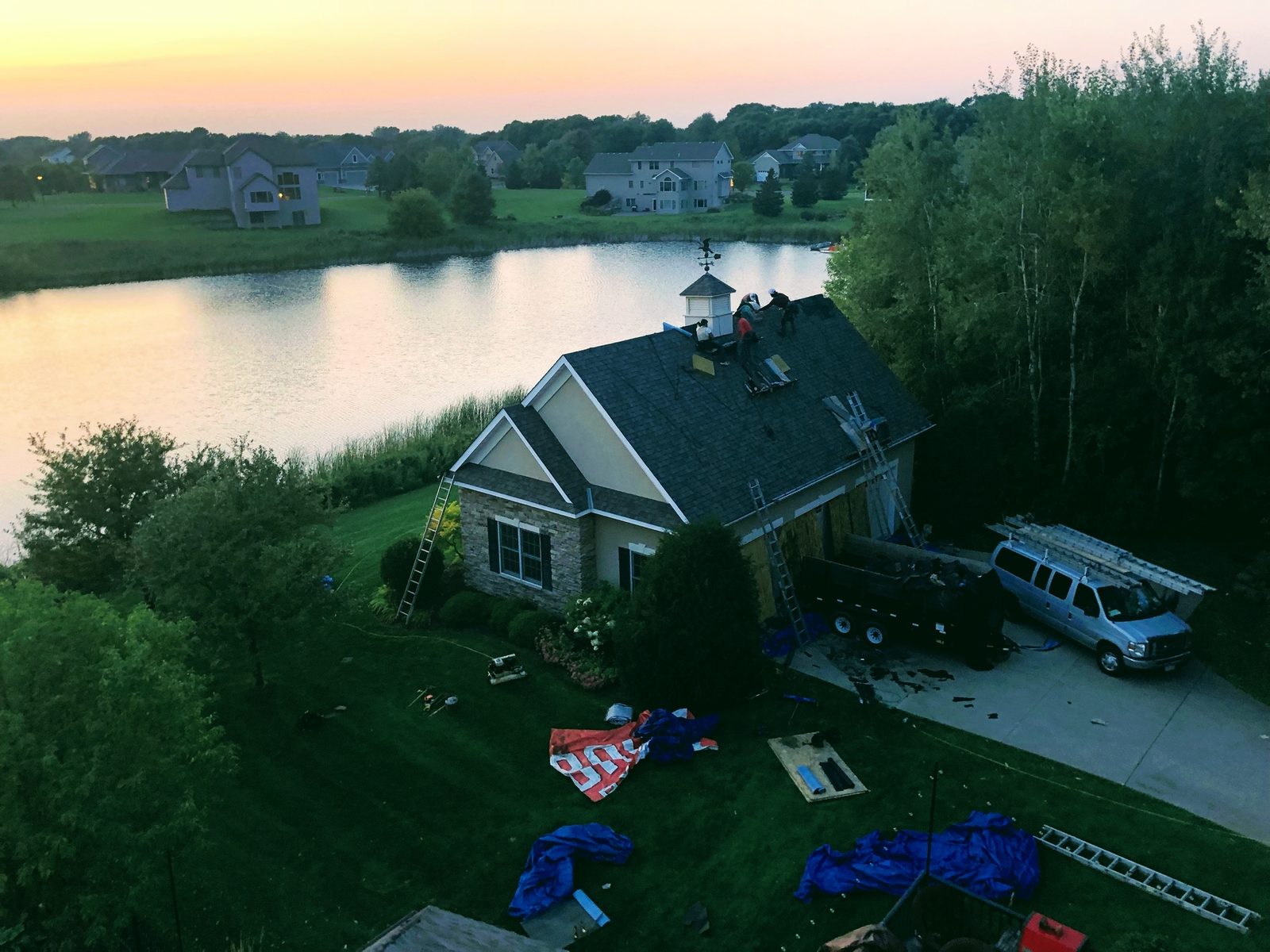 Aerial drone view at sunset of a lakefront estate with a newly completed shingle roof by Roofs R Us
