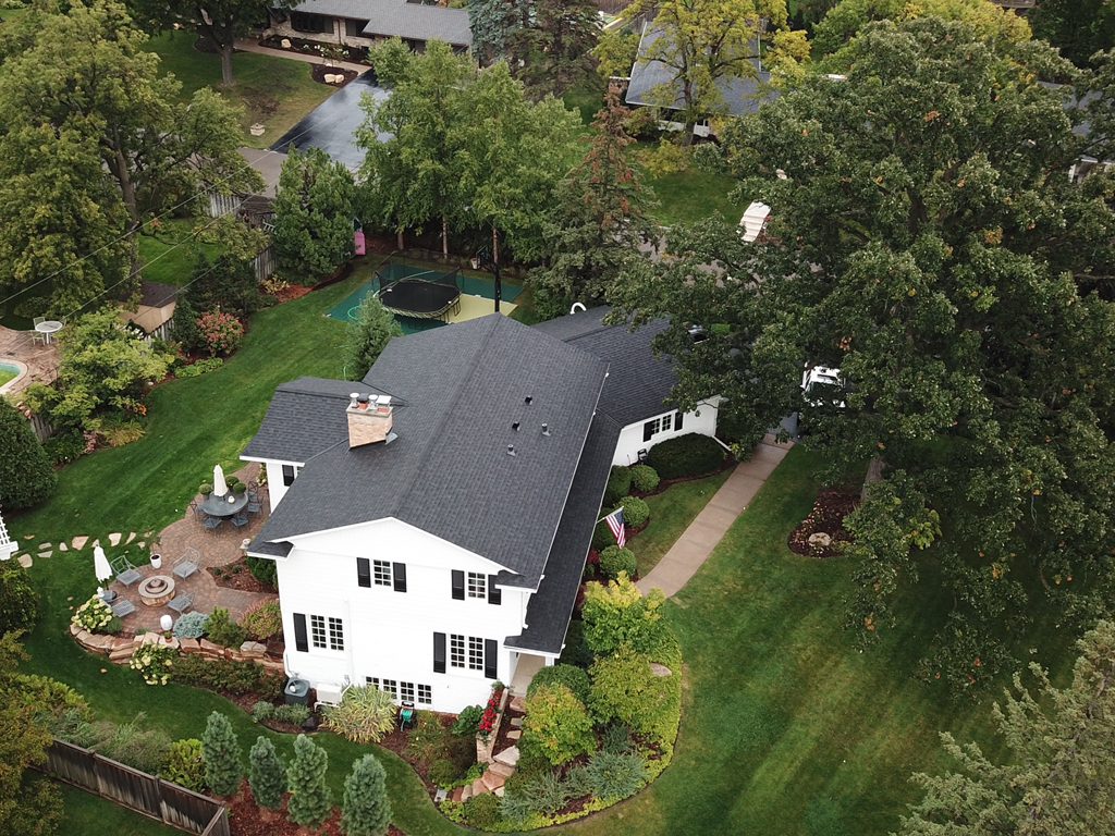 Aerial drone view of a white colonial house with a new dark shingle roof