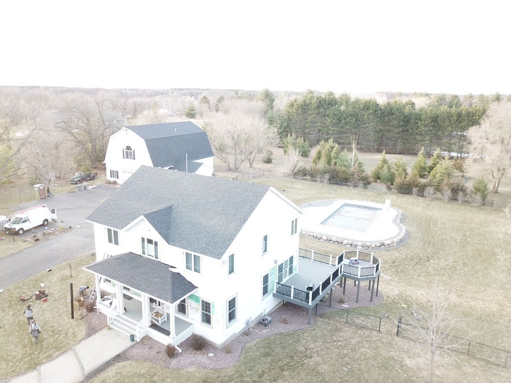 Aerial drone view of a white farmhouse with a new gray shingle roof and a pool alongside it