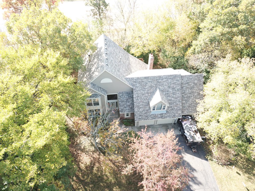Aerial drone view of a home on a wooded lot with a new shingle roof and a rebuilt chimney flashing detail