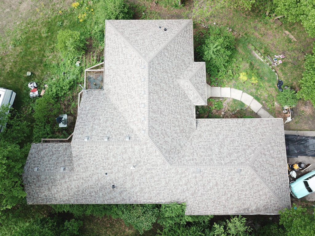 Aerial drone view of a hillside home with a new light gray architectural shingle roof