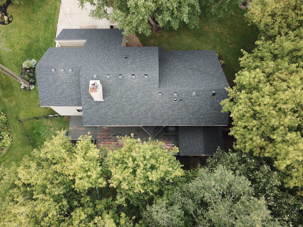 Aerial drone view of a home surrounded by woods with a new gray architectural shingle roof