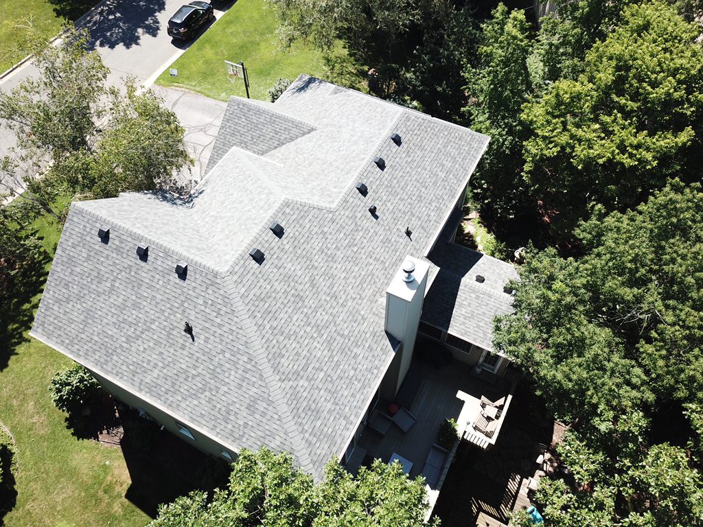 Aerial drone view of a new gray shingle roof on a house set into a wooded lot