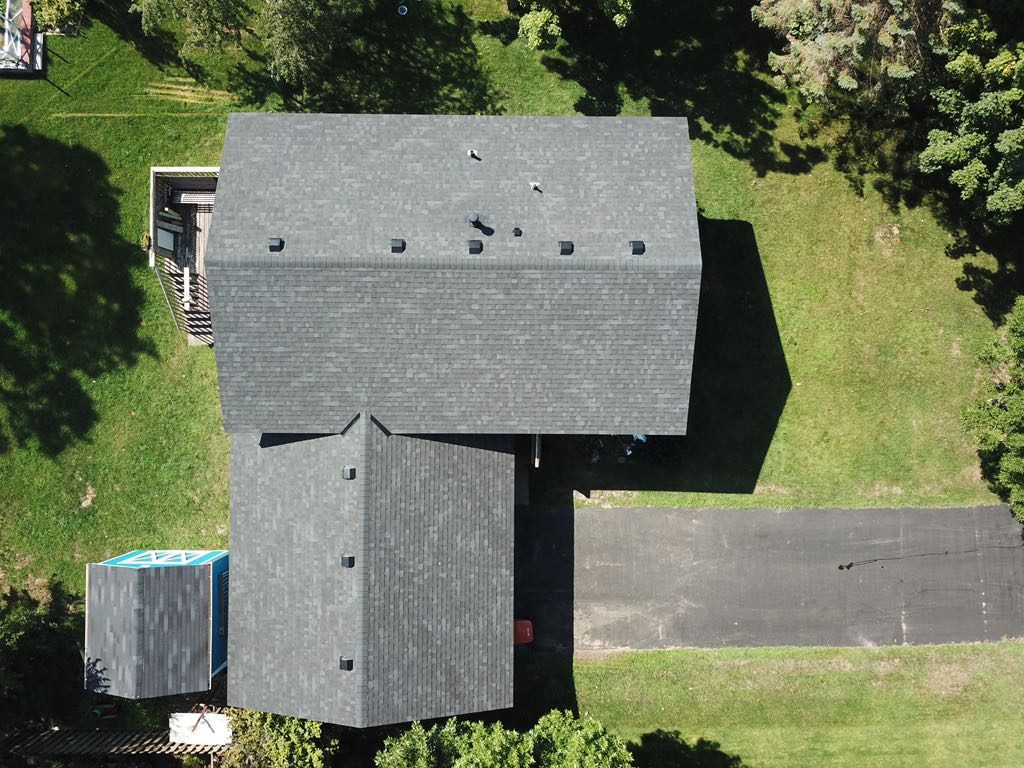 Aerial drone view of a house with a new gray shingle roof and a large open backyard