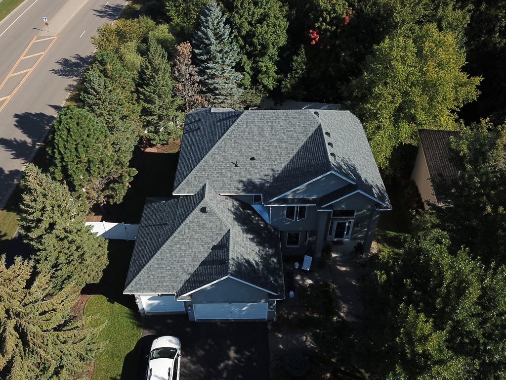 Aerial drone view of a large home with a new charcoal shingle roof surrounded by mature trees