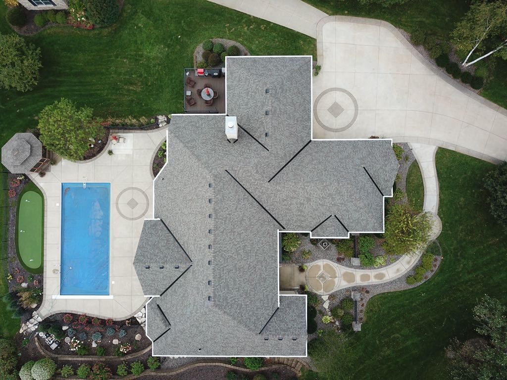 Aerial drone view of a luxury home with a new shingle roof, swimming pool and patio