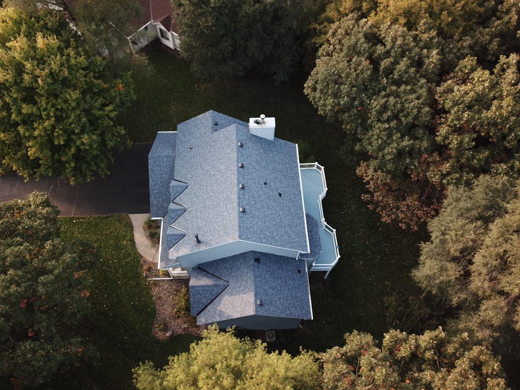 Aerial drone view of a home with a new gray shingle roof nestled among trees