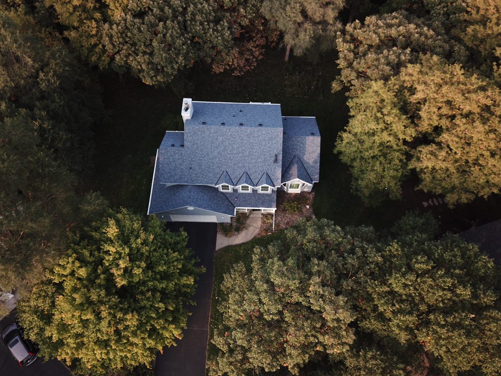 Aerial drone view of a dark gray shingle roof on a home surrounded by fall foliage