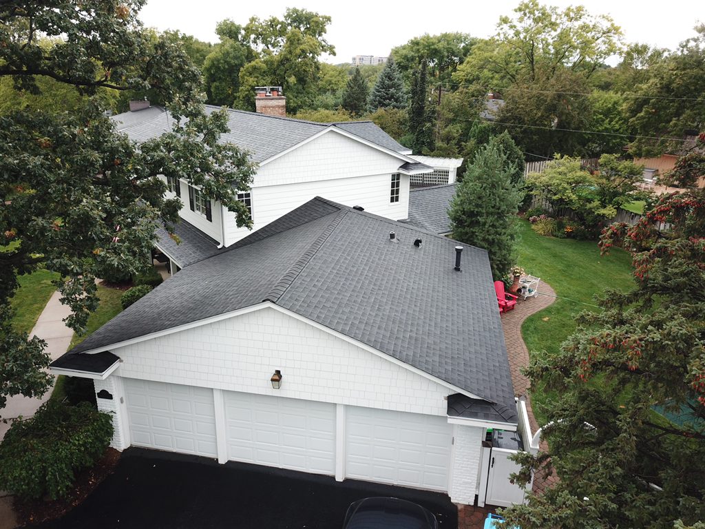 Aerial drone view of a white home with a new charcoal shingle roof covering the house and attached garage