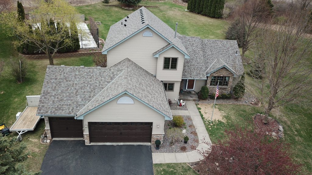 Aerial drone view of a two-story home with a new gray shingle roof and a swept driveway after cleanup