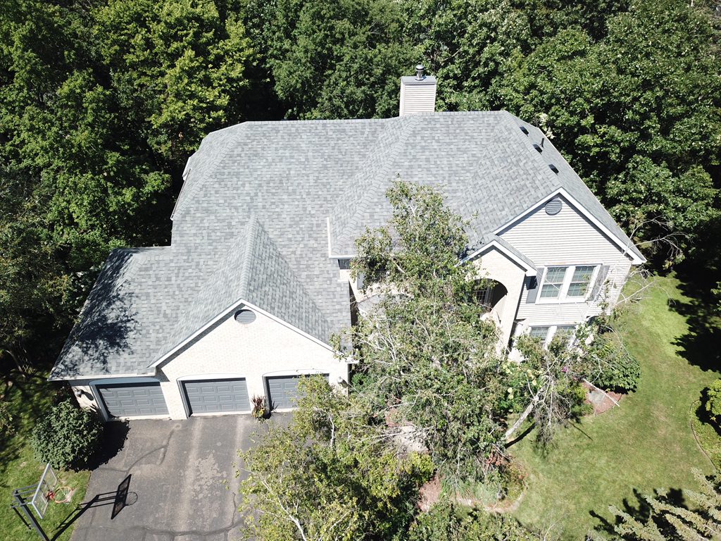 Aerial drone view of a large home finished with a light gray architectural shingle roof