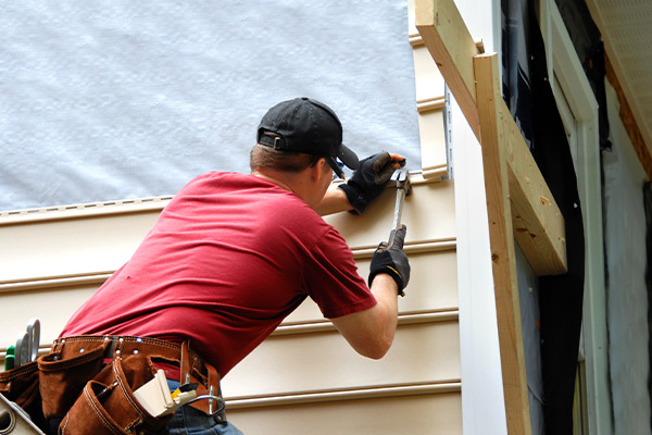 Roofs R Us worker installing vinyl siding on a new construction home