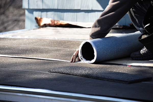 Roofer laying out tar paper on a roof that was damaged in a storm