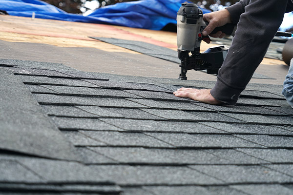 Roofer nailing down shingles after storm damage repair in Minneapolis.