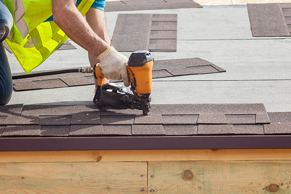 Roofer installing new brown shingles on a remove that was damage by a storm in Woodbury, MN