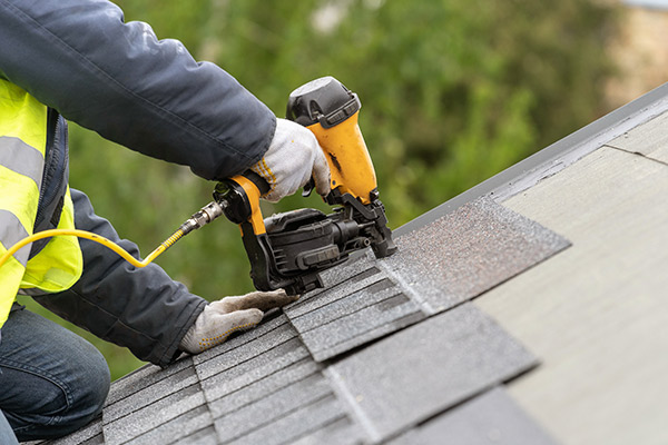 a person using a nail gun to install shingles